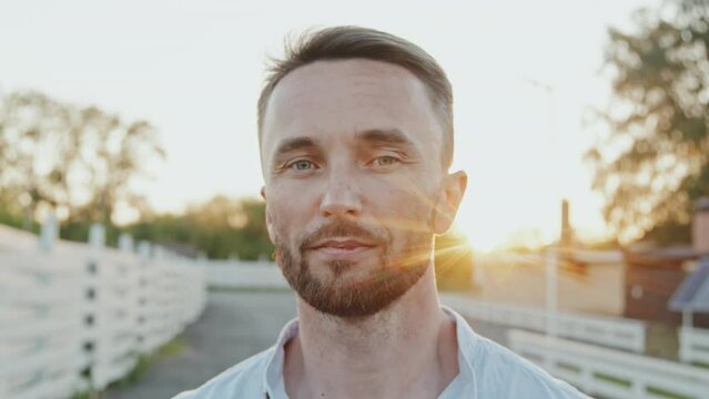 Close-up of handsome blue-eyed Caucasian man smiling and looking on camera outdoors on sunset in summer