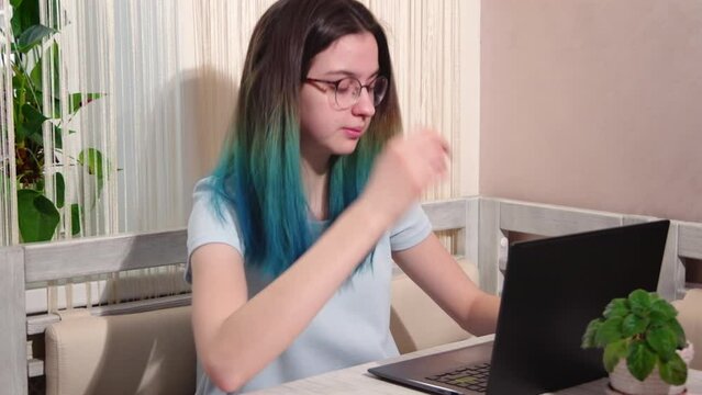Tired teenage girl looking at a laptop while sitting at the table. Overwork during study, preparation for exams.
