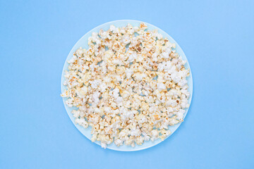 Popcorn on a turquoise plate for watching a movie. Blue background. Copy space. Flat lay. Top view. Quick and tasty snack