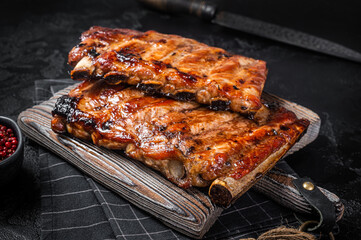 Obraz na płótnie Canvas Stack of grilled pork ribs in BBQ sauce on a chopping board. Black background. Top view