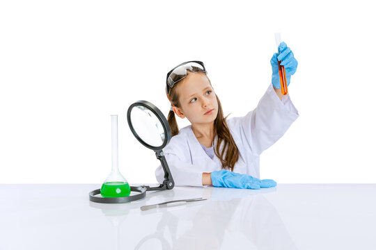 Portrait of little school girl, kid in white big gown as chemist, scientist doing experiment with multicolored chemical fluid in laboratory isolated on white background