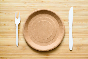 Empty brown paper plate and fork with knife on a wooden table. View from above. Eco-friendly disposable tableware. copyspace.