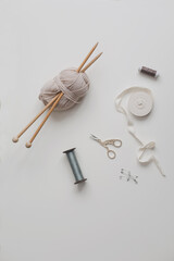 Top view of scissors, threads, knitting needles and sewing supplies on a white background. Concept of craft hobby, knitting and sewing.