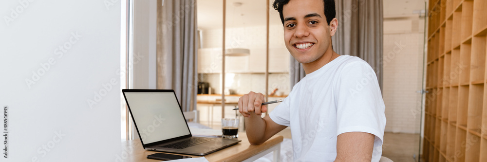 Wall mural smiling young hispanic man working studying on laptop