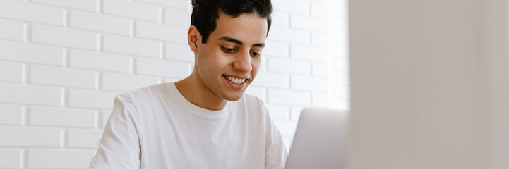 Obraz premium Smiling young hispanic man working studying on laptop