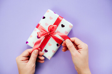 Hands untying a ribbon bow on a gift box wrapped in heart pattern paper