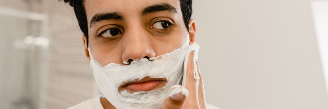 Smiling Young Hispanic Man Shaving His Face Standing