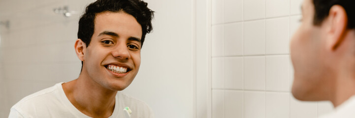 Smiling young hispanic man brushing teeth