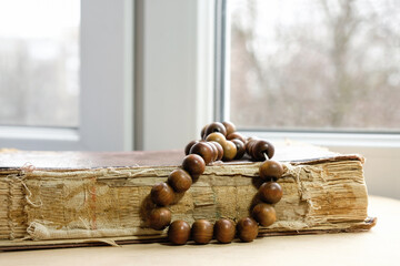 Old book and wooden rosaries at home on the windowsill on a cloudy day.