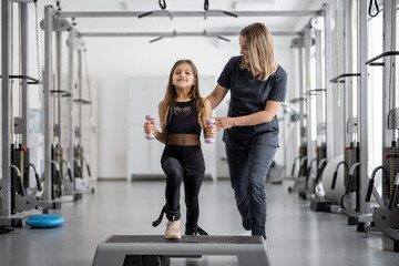 Rehabilitation specialist helping little girl to do exercises at gym. Concept of physical therapy...