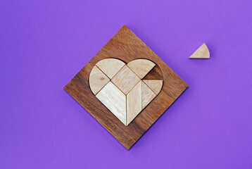 Wooden puzzle details in wooden heart-shaped box with missing piece on purple background