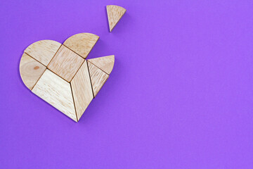 Wooden heart puzzle with missing piece on purple background