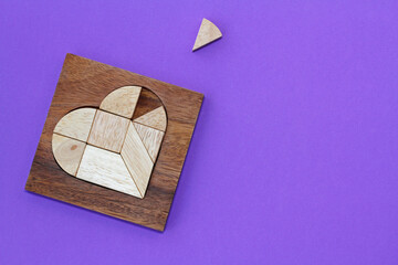 Wooden puzzle details in wooden heart-shaped box with missing piece on purple background