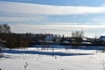 A frosty clear winter day. View of a snow-covered field and a village or cottages in the distance