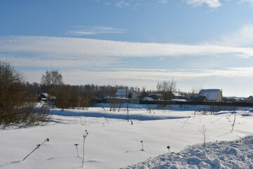 Fototapeta na wymiar A frosty clear winter day. View of a snow-covered field and a village or cottages in the distance