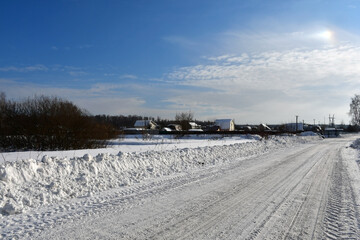 Fototapeta premium A frosty clear winter day. View of the snowy road leading to the village or country village, rural houses in the distance