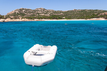 inflatable boat tied to a boat leaving a beach in turquoise waters
