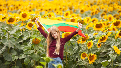 Girl holding flag of Lithuania in a sunflowers field. Lithuanian Flag Day. Independence restoration...