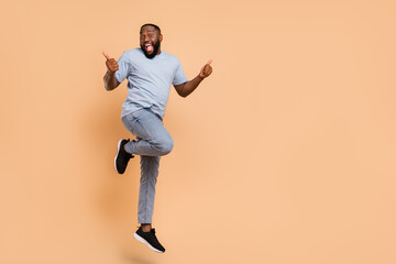 Fototapeta na wymiar Full length body size view of attractive cheerful cool guy jumping showing thumbup isolated over beige pastel color background