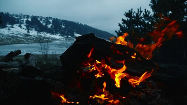 campfire burning at sunset against frozen lake view in winter camp