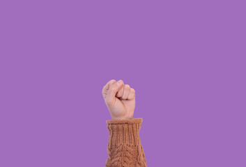 woman's fist on lilac background representing victory, touching the clouds