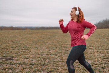 Happy sportive woman listening to music on headphones while jogging in nature. Weight loss concept