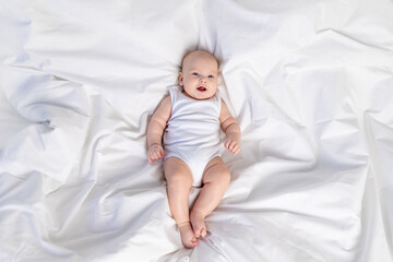 baby on the white bed on the bed in the morning. Textiles and bed linen for children. A newborn baby has woken up or is going to bed