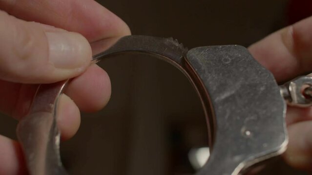Close-up of handcuffs in the rapist hands. Sustained fear for safety concept. Dark background.