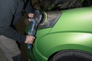 Polishing car headlights. Car service worker with electrical polisher polishing hood in auto repair shop