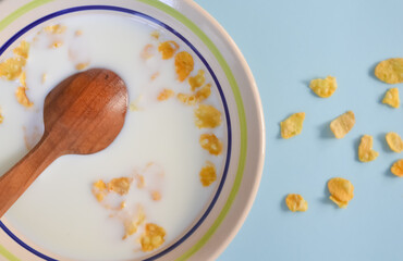 Wooden spoon inside a bowl with cornflakes and milk on a blue surface