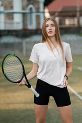 Girl athlete in a white T-shirt and black tight shorts with a racket on the tennis court. Fashion and sport concept.