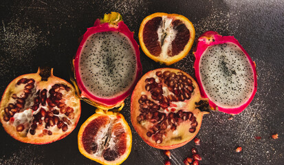 Split open dragon fruit, blood orange, and pomegranate fruit.  With dark textured background. 