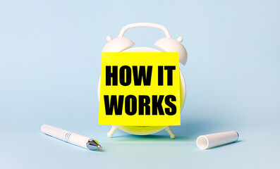 On a light blue background - a white handle and an alarm clock with a bright yellow sticker glued to it with the text HOW IT WORKS