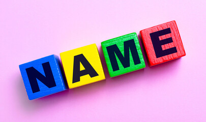 On a light pink background, multi-colored wooden cubes with the text NAME