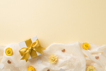 Top view photo of woman's day composition white giftbox with yellow bow yellow and white wild flowers and hearts on white soft textile on isolated beige background with copyspace