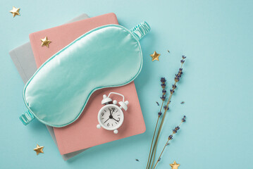 Top view photo of blue silk sleeping mask small white alarm clock on diaries golden stars and sprig...
