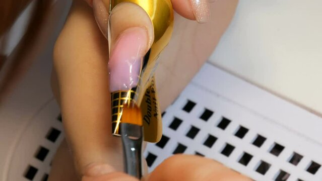 A special acrylic texture is applied to the nail and corrects the shape of the nail on a special stencil. Nail extension service. Manicurist makes a manicure Gel Nail extension close up view
