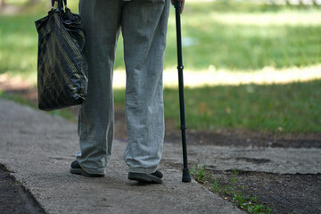 The legs of an elderly man with an uncertain gait, leaning on a cane and walking along the path...