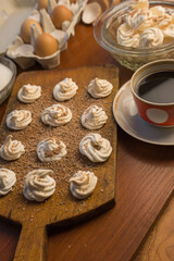 Delicious crispy homemade egg meringue sprinkled with grated dark chocolate, prepared with love on a wooden background, crunchy dessert for coffee or tea.

