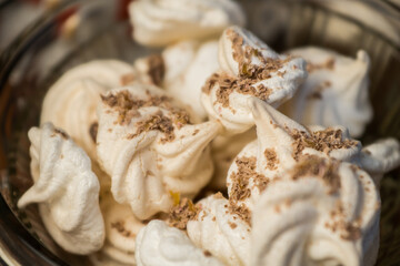 Delicious crispy homemade egg meringue sprinkled with grated dark chocolate, prepared with love on a wooden background, crunchy dessert for coffee or tea.
