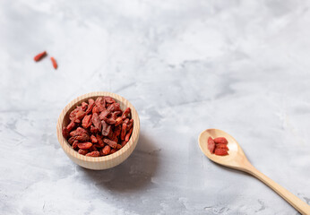a wooden bowl with goji berries and a wooden spoon on a concrete table. A place to copy. Selective focus.