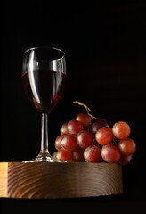 A glass of red wine and a bunch of grapes on a wooden table top. Selective focus.