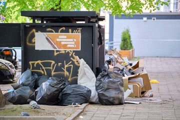 Garbage bins disposal full with litter scattered around on city street © bilanol