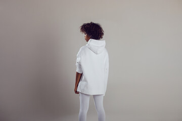 African American woman with puffy hair in a white hoodie and leggings stands on a white background...