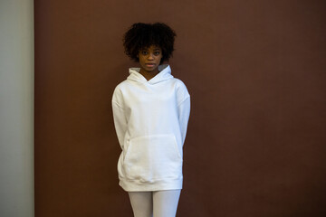 African american woman in a white hoodie and leggings stands on a brown background. Mock-up.