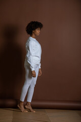 Fototapeta premium African-American girl in a white sweatshirt and leggings stands on a brown background. Mock-up.