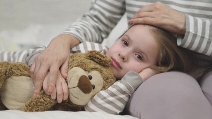 Small girl hugs teddy bear lying on mother lap before sleep