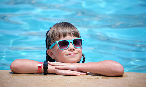 Portrait of happy child girl relaxing on swimming pool side on sunny summer day during tropical holidays