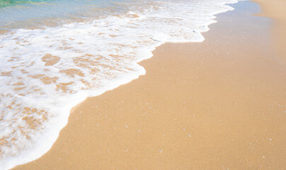 White foam of the sea wave on the white sand of the beach. Bright sea beach background. Light blue ocean wave on the sand.