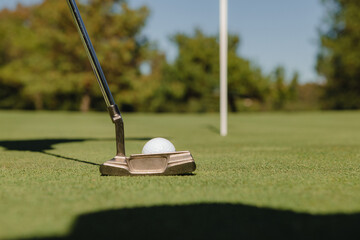Detail of golf club about to hit the ball on the green